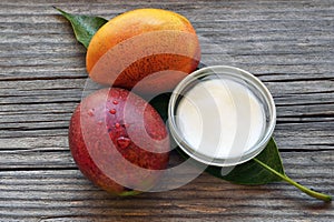 Mango body butter in a glass bowl and fresh ripe organic mango fruits on old wooden background.Spa,natural oils,organic cosmetic o