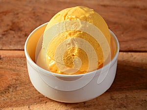 Mango ice cream scoops served in a white bowl over a rustic wooden table, selective focus