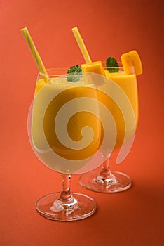 Mango Lassi or smoothie in big glass with mint leaf. Side angle Isolated over colourful background