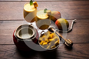 Mango Lassi or smoothie in big glass or small bottles with curd, cut fruit pieces and blender.
