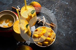 Mango Lassi or smoothie in big glass or small bottles with curd, cut fruit pieces and blender.