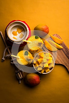 Mango Lassi or smoothie in big glass or small bottles with curd, cut fruit pieces and blender.