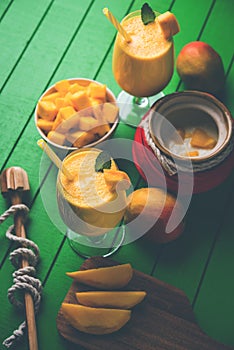 Mango Lassi or smoothie in big glass or small bottles with curd, cut fruit pieces and blender.