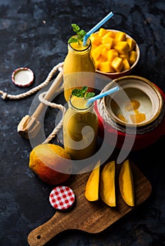 Mango Lassi or smoothie in big glass or small bottles with curd, cut fruit pieces and blender.