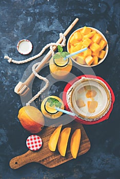 Mango Lassi or smoothie in big glass or small bottles with curd, cut fruit pieces and blender.