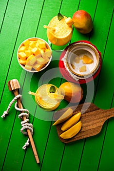 Mango Lassi or smoothie in big glass or small bottles with curd, cut fruit pieces and blender.