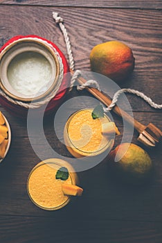 Mango Lassi or smoothie in big glass or small bottles with curd, cut fruit pieces and blender.