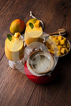 Mango Lassi or smoothie in big glass or small bottles with curd, cut fruit pieces and blender.