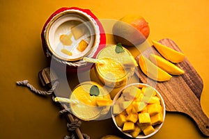 Mango Lassi or smoothie in big glass or small bottles with curd, cut fruit pieces and blender.