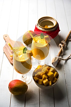 Mango Lassi or smoothie in big glass or small bottles with curd, cut fruit pieces and blender.