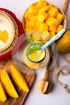 Mango Lassi or smoothie in big glass or small bottles with curd, cut fruit pieces and blender.