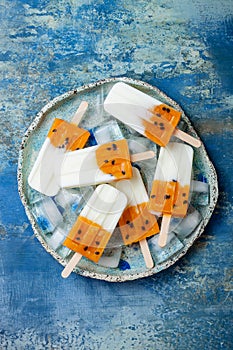 Mango passion fruit popsicles with coconut cream on ice cubes over blue plate.