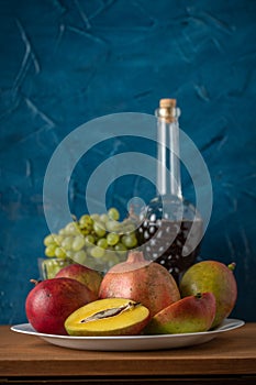 Mango, pomegranate, grapes and a bottle of wine. Still life on a blue background