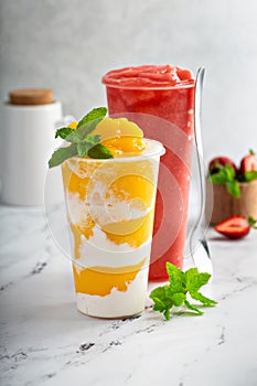 Mango smoothie with whipped coconut cream swirled in a tall cup and strawberry smoothie