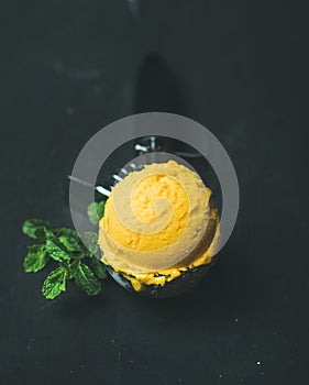 Mango sorbet ice cream scoop in scooper over black background