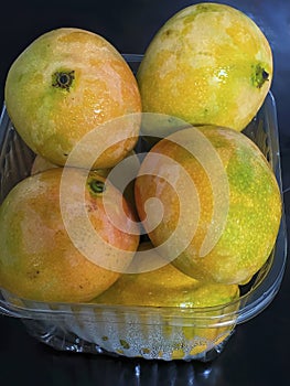 Mango with water drops in plastic box on table