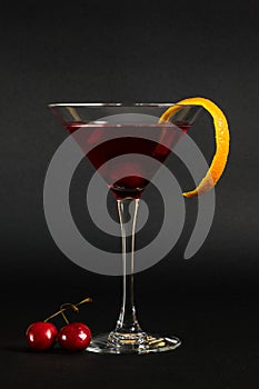 Manhattan cocktail a classic mixed drink aperitif with cherries and orange peel on black background.