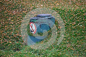 Manhole with a forbidding sign on the Bank in green grass and yellow leaves