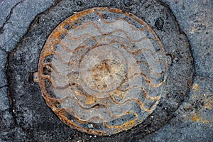 Manhole with rusty metal cover in cracked asphalt surface