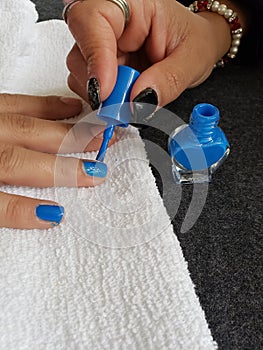 woman painting the fingernails of another woman with blue nail polish photo
