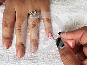 woman painting the fingernails of another woman with light pink nail polish photo