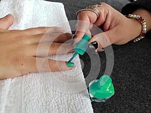 woman painting the fingernails of another woman with aquamarine nail polish photo