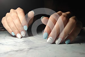 Manicure with glossy blue solid coating and marble design.