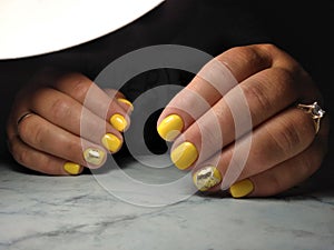 Manicure with a glossy yellow coating. the design of golden hearts with sparkling flakes