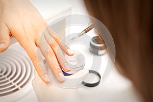 Manicure master applying acrylic powder on the female nails in a beauty salon. Strengthening of nails acrylic powder.