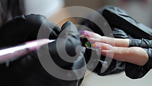 A manicure master in black gloves gives a manicure to a girl. Close-up of a beautician's hand painting a woman's nails