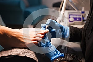 Pedicure master polishes nails with nail file drill before applying varnish side view