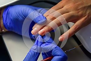 Manicure master in gloves apply base coat to the client`s nails. Manicure in the salon, close up. Beauty and care of hands