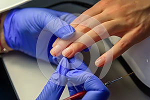 Manicure master in gloves apply base coat to the client`s nails. Manicure in the salon, close up. Beauty and care of hands