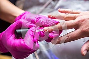 Manicure master in pink gloves scraping off the old coat of varnish in manicure salon using drill.  Professional manicure in