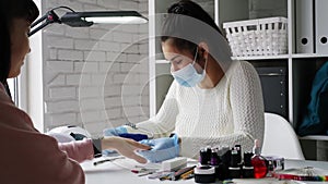 Manicure master in rubber gloves and mask talking with the client in beauty studio interior