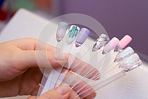 Manicure and nail care concept. A woman in a beauty salon holds colored test nail polishes with different colors and chooses the photo