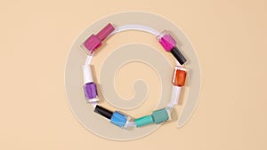 Manicure nail polishes bottles appear in circle with copy space on beige background. Stop motion flat lay