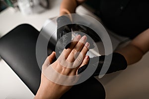 Manicure procedure in beauty salon. Master in black gloves and the hands of the client. Close-up. Top view