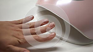 Manicure salon client holding hand in LED lamp, drying gel nail polish, beauty