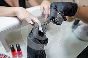 Manicure salon master removes cuticles with nail scissors. Woman getting nail manicure. Professional manicure in beauty salon.