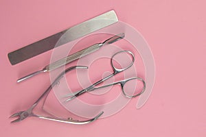 Manicure scissors, saw and nail bag as well as cuticles cutters standing on a pink background