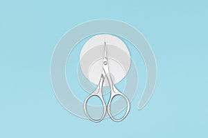 Manicure scissors on white cotton pad on blue background. Nails care equipment. Stainless steel scissors on blue background