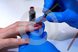 Manicure specialist applying red nail polish on healthy natural female nails