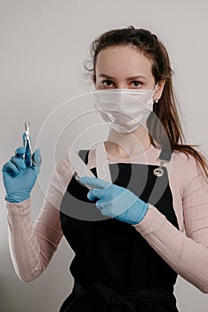 Manicure tools in hands of female manicurist wearing mask and gloves