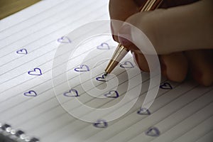 A manicured female hand draws many hearts in notebook