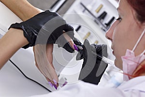 A manicurist applies a violet gel with a brush on the client`s nails close-up. photo