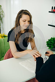 Manicurist applying cuticle softener or clear nail varnish to the fingernails of a lady client in a spa or beauty salon