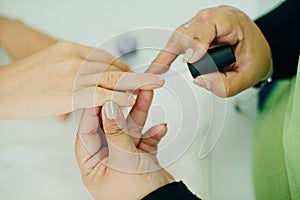 Manicurist applying cuticle softener or clear nail varnish to the fingernails of a lady client in a spa or beauty salon