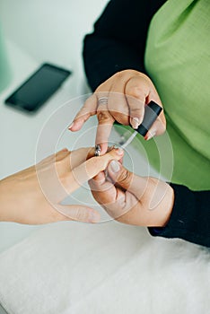 Manicurist applying cuticle softener or clear nail varnish to the fingernails of a lady client in a spa or beauty salon