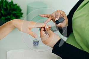 Manicurist applying cuticle softener or clear nail varnish to the fingernails of a lady client in a spa or beauty salon